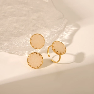 Boucles d'oreilles pierre beige et bague dorée réglable sur une surface blanche texturée