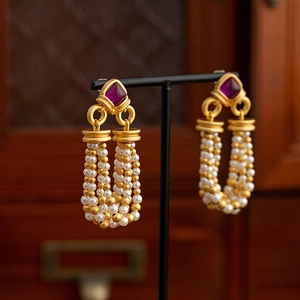 Vintage gold tassel earrings with purple gemstone and pearls on a black display stand