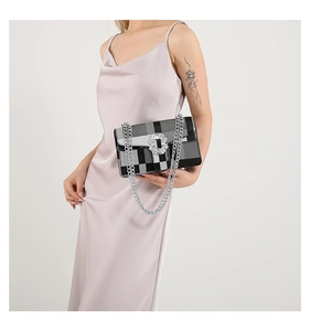 Model holding a black checkerboard shoulder bag with a large rhinestone buckle and silver chain