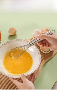 Close-up of stainless steel whisk stirring egg yolks in a ceramic bowl on a wooden tray
