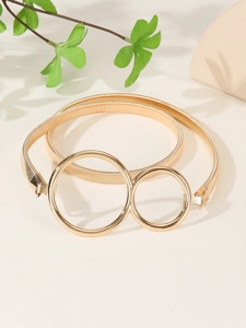 Detail of a golden metal spring belt featuring a minimalist double ring buckle design