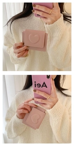 Pink heart-embossed short wallet held by model against a soft knit sweater background