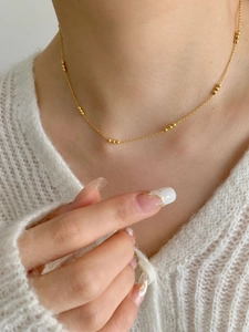 Close-up of golden beaded chain necklace worn on the collarbone for a minimalist look