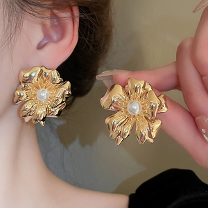 Detail of golden floral earrings with white pearls on a model showing petal texture
