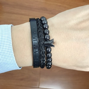 Close-up of black matte roman numeral cuff, woven bracelet, and crown bead set