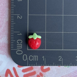 Detailed view of a mini 1cm red resin strawberry charm on a centimeter measurement scale
