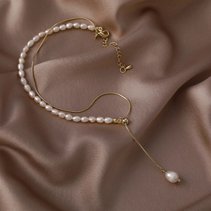 Detail of a layered baroque pearl necklace with gold snake chain on champagne silk