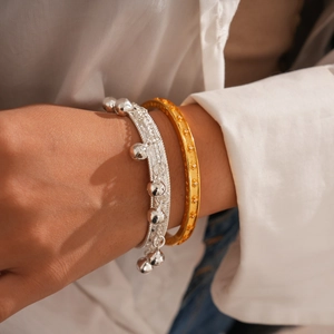 Détail d'un jonc doré avec motifs étoiles et d'un bracelet tressé à breloque argentée