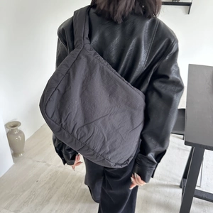 Detail view of the black oversized puffy tote bag worn by a model in a minimalist room