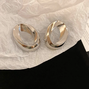 Detail of silver oval twist knot earrings resting on white textured paper backdrop