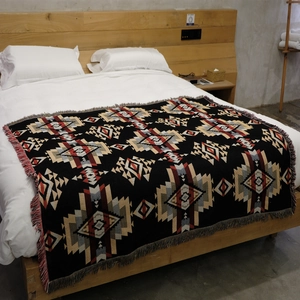 Bohemian geometric woven camping blanket with tassels displayed on a minimal bed