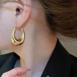 Detailed close-up of large golden U-shaped hoop earrings with a mirror polished finish