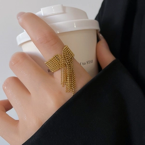 Detail of gold-plated beaded tassel ring on model holding a white coffee cup