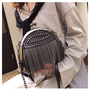 Detail of black rivets and long metallic fringes on a leather shell-shaped crossbody bag