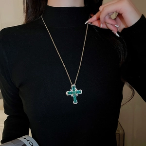Gros plan sur un collier croix dorée avec pierres vertes carrées et petits diamants