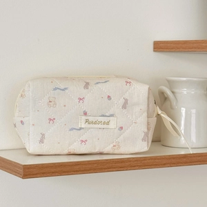 Detail view of cream quilted makeup bag with brown bear and bunny patterns and ribbon puller