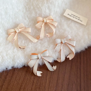 Close-up of enamel bow earrings in creamy white and beige on soft velvet background