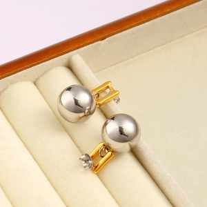 Close-up of gold H-shaped connector and silver spherical earring on beige velvet
