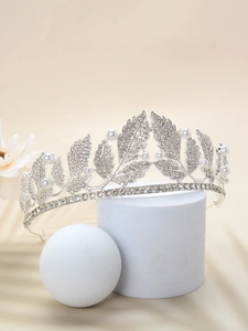 Detail of silver bridal tiara featuring rhinestone leaves and elegant pearls on a pedestal