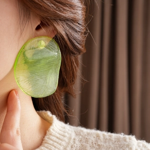 Close-up of irregular round earrings in yellow-green resin with a brushed texture
