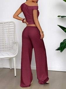 Detail of burgundy textured two-piece set featuring a one-shoulder top and wide-leg pants
