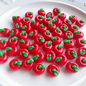 Close-up of red resin apple charms with green leaves on a white ceramic plate