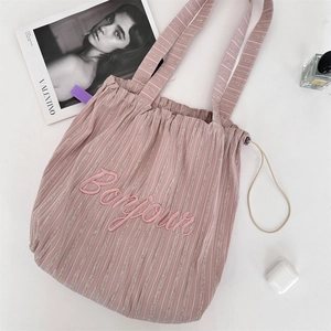 Detail of pink striped canvas tote bag featuring embroidered Bonjour text with lifestyle props