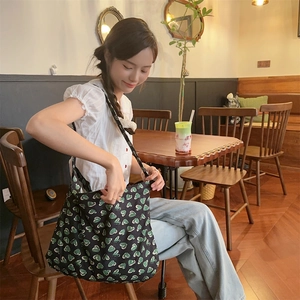 Model wearing a large floral canvas tote bag with green heart patterns in a cozy cafe