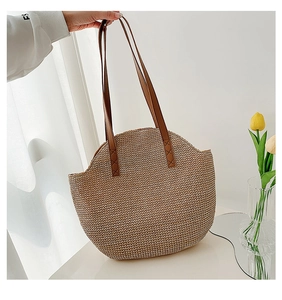 Detail of hand-woven straw tote with premium brown leather handles and reinforced stitching