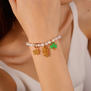 Elegant gold pearl bracelet with clover, starfish, and leaf charms on a wrist