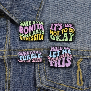 Set of four colorful enamel pins with fun English phrases on a blue denim jacket background