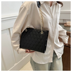 Detail view of black quilted chain strap bag worn by model in minimalist setting