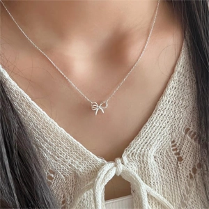 Close-up of minimalist S925 silver bow pendant necklace worn by a model in soft light