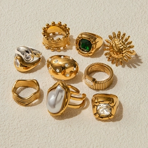 Vintage gold-plated rings with irregular pearls and green emerald stones set on stone background
