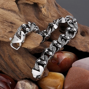 Detailed view of silver Cuban link bracelet with skull charms on weathered wood and pebbles