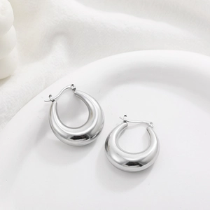 Detailed close-up of thick silver hollow hoop earrings displayed on a white ceramic dish