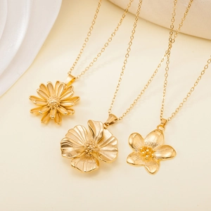 Detailed view of three gold flower pendant necklaces on a minimalist beige background