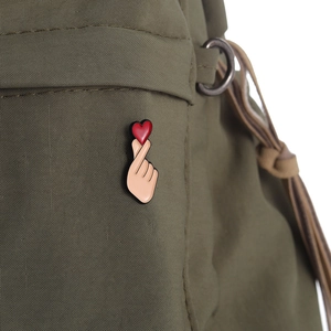 Detail of finger heart enamel pin with red heart on olive green canvas fabric