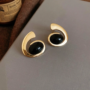 Macro shot of vintage gold spiral earrings with black oval gemstone on a grey book cover