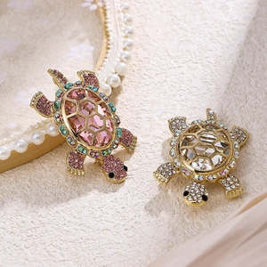 Macro detail of two crystal turtle brooches with pink and clear gemstones on a soft fabric