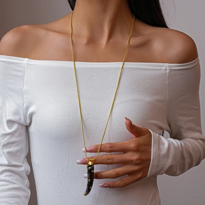 Close-up of a black cornicello horn pendant with gold studs on a long gold chain