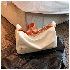 Detail einer weißen zylindrischen Tasche mit leuchtend orangem Schultergurt und Anhänger