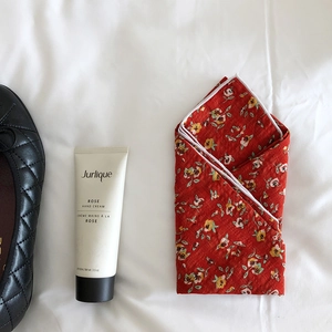 Detail view of a folded red floral linen scarf paired with rose hand cream