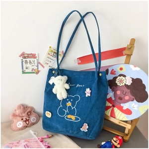 Close-up of blue corduroy tote bag featuring bear embroidery and cute plush charms