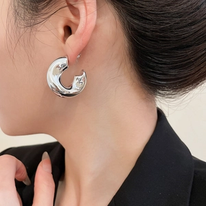 Close-up of a silver C-shaped chunky hoop earring on a model with a polished finish