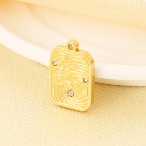 Macro shot of gold square pendant with wave pattern and tiny crystals on fabric