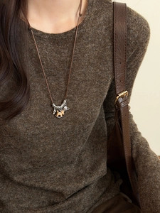 Detail view of tiger eye horse pendant on pearl necklace styled with a brown sweater