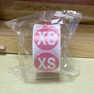 Detailed view of round pink size XS adhesive labels on a roll in transparent packaging