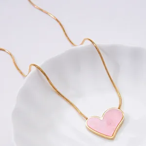 Elegant gold titanium necklace with a pink resin heart pendant on white ceramic plate