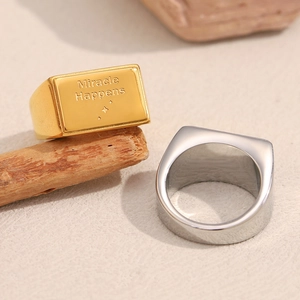 Dettaglio degli anelli quadrati in oro e argento con l'incisione 'Miracle Happens'